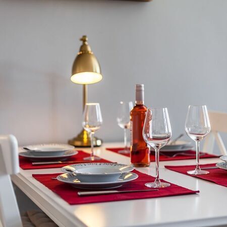 Appartement Lolita - Eleganter Esstisch mit rotem Tischset und Weingläsern