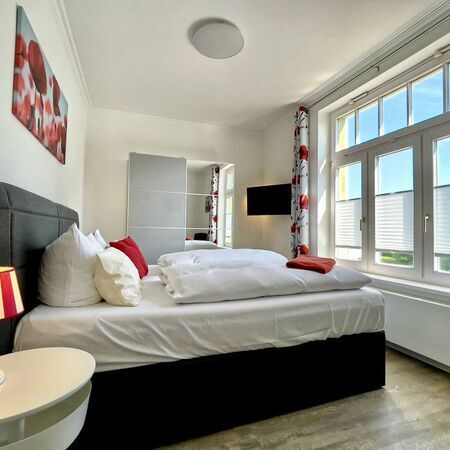 Appartement Kronenburg - Komfortables Bett mit weißen Bettwäsche und roten Akzenten im Schlafzimmer