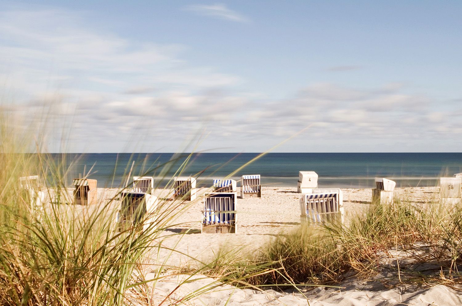 Ein Strand fotografiert aus den Dünen mit Strandkörben und dem Meer im Hintergrund